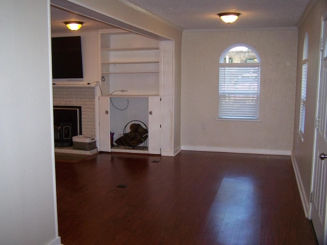 unfurnished living room featuring dark wood-type flooring, ornamental molding, built in shelves, and a textured ceiling