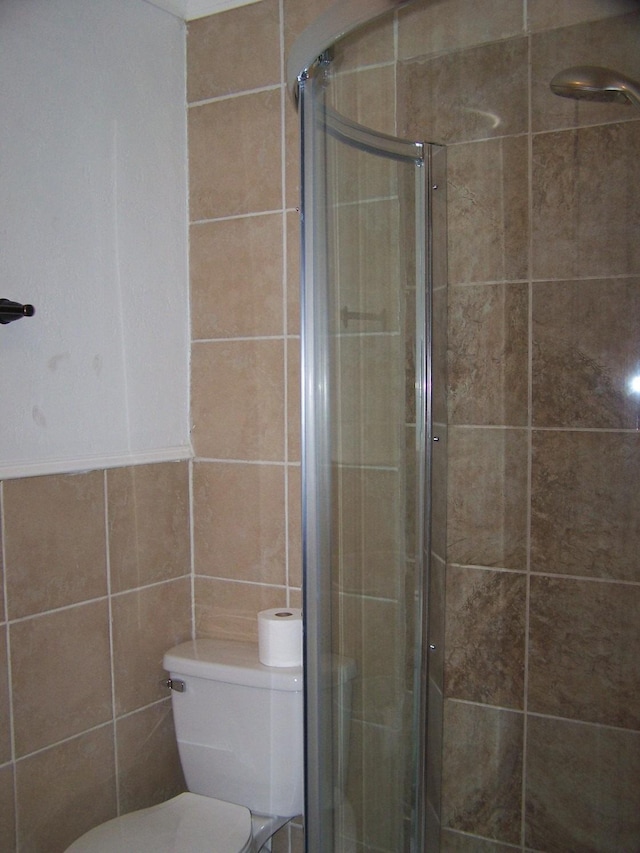 bathroom with tile walls, a shower with door, and toilet