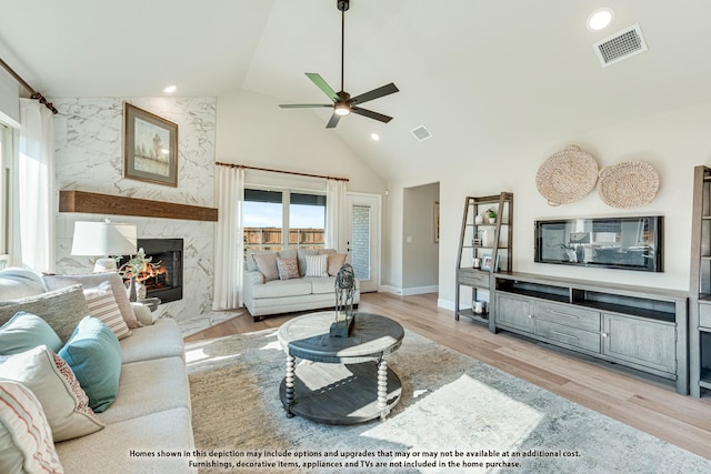 living room featuring high vaulted ceiling, ceiling fan, light wood-type flooring, and a high end fireplace