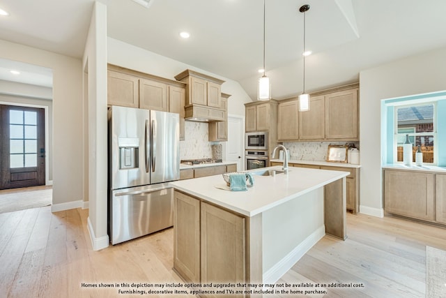 kitchen featuring appliances with stainless steel finishes, a center island with sink, light brown cabinets, and decorative light fixtures