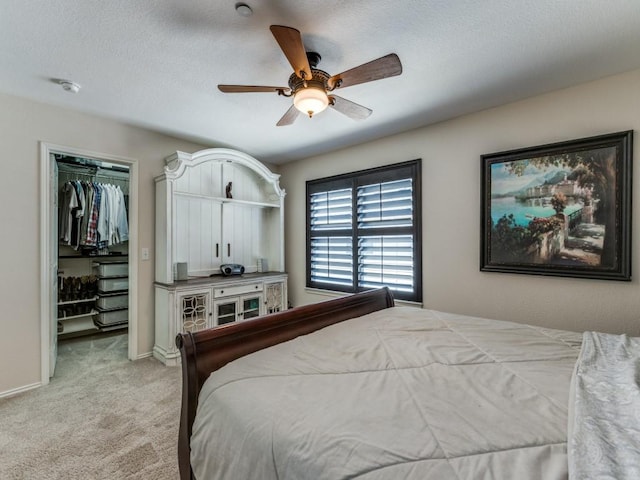 bedroom with ceiling fan, a textured ceiling, a walk in closet, light colored carpet, and a closet