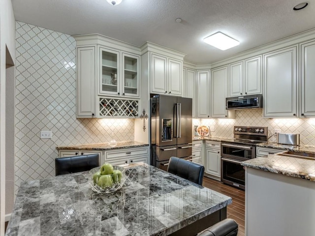 kitchen featuring a breakfast bar, stone countertops, appliances with stainless steel finishes, decorative backsplash, and white cabinets