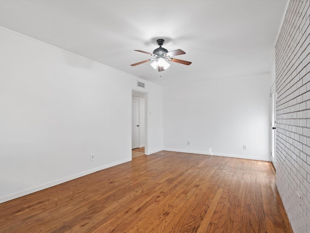 empty room with hardwood / wood-style flooring, ceiling fan, and brick wall