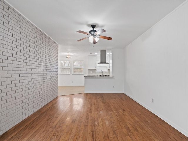 unfurnished living room with sink, ceiling fan, light wood-type flooring, ornamental molding, and brick wall