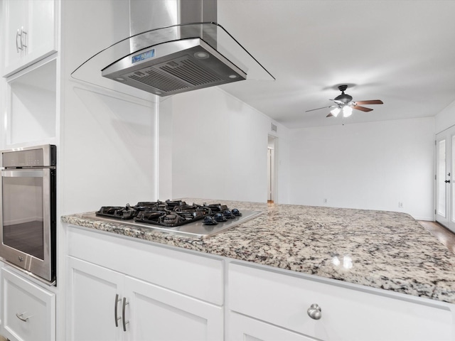 kitchen featuring ceiling fan, light stone countertops, appliances with stainless steel finishes, island range hood, and white cabinetry