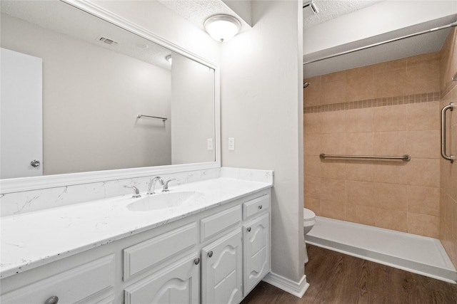 bathroom with wood-type flooring, a textured ceiling, tiled shower, toilet, and vanity