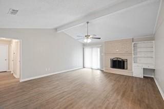 unfurnished living room with ceiling fan, a fireplace, lofted ceiling with beams, and dark hardwood / wood-style floors