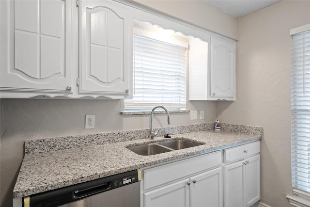 kitchen with light stone counters, sink, white cabinets, and stainless steel dishwasher