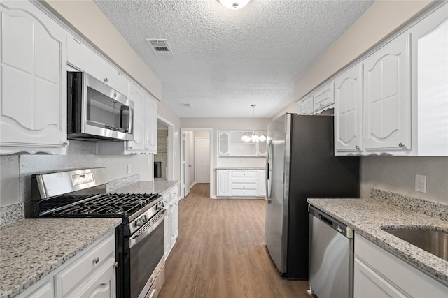 kitchen with light wood-type flooring, stainless steel appliances, decorative light fixtures, a notable chandelier, and white cabinets