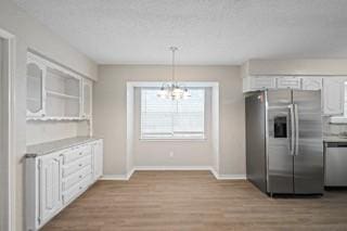 kitchen with hanging light fixtures, stainless steel appliances, light hardwood / wood-style flooring, a notable chandelier, and white cabinets