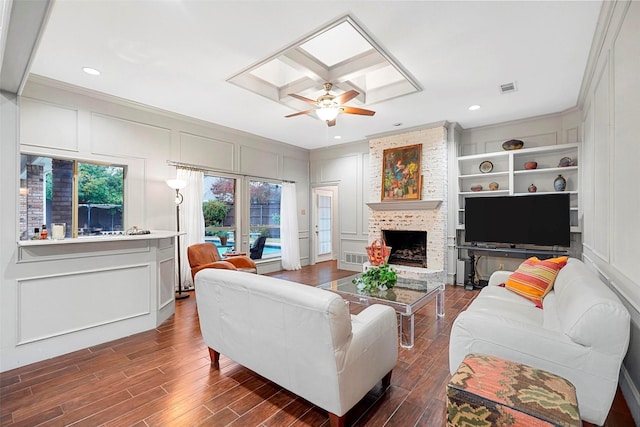 living room featuring wood-type flooring, built in shelves, a fireplace, and a skylight