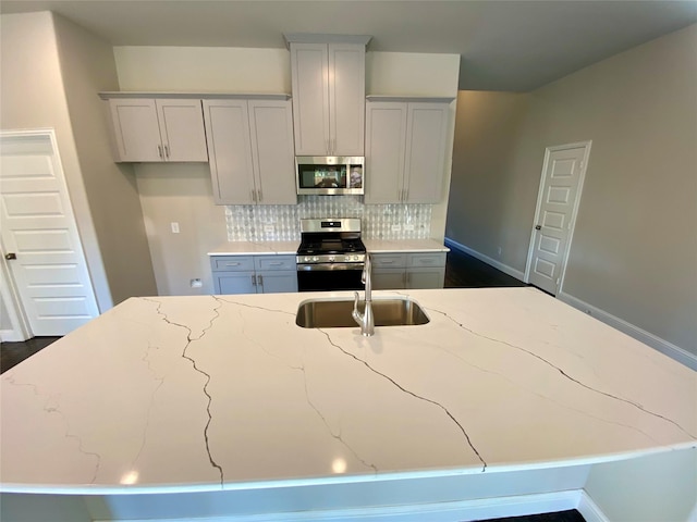 kitchen with sink, stainless steel appliances, tasteful backsplash, light stone counters, and a kitchen island with sink