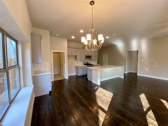 kitchen with appliances with stainless steel finishes, backsplash, dark hardwood / wood-style flooring, decorative light fixtures, and a center island with sink