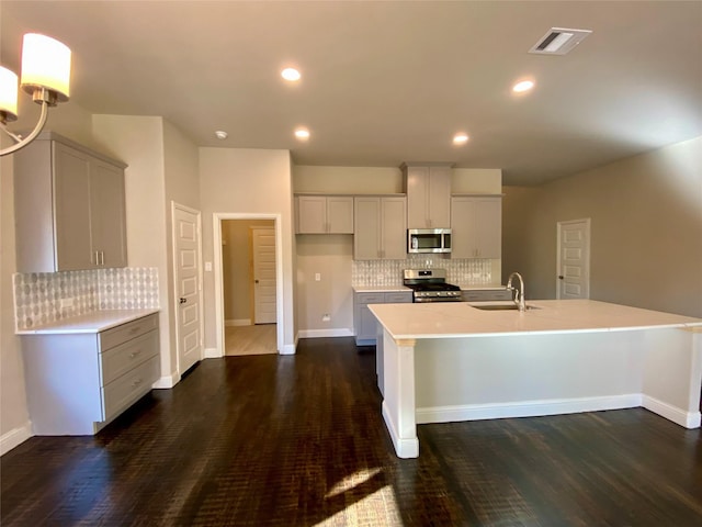 kitchen with appliances with stainless steel finishes, a kitchen island with sink, dark wood-type flooring, and sink