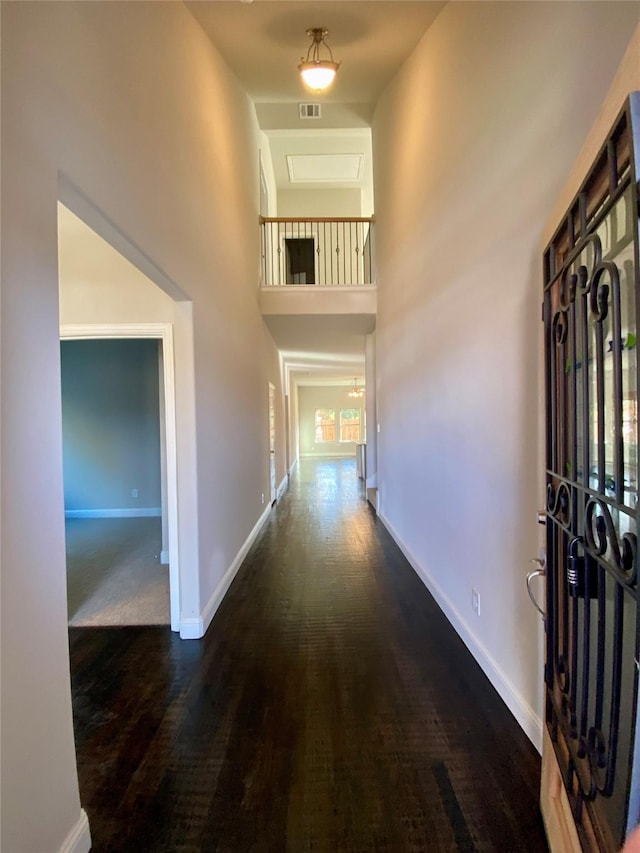 hallway featuring a towering ceiling, visible vents, baseboards, and wood finished floors