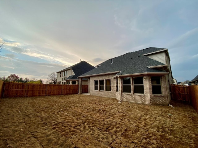 back of house with a fenced backyard, a shingled roof, and brick siding