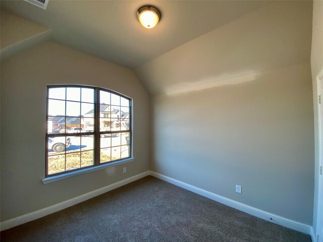 spare room with dark colored carpet, vaulted ceiling, and baseboards