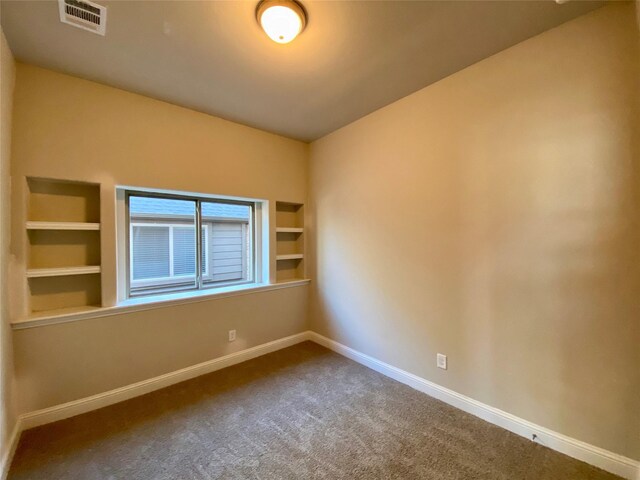 carpeted empty room with built in features, visible vents, and baseboards