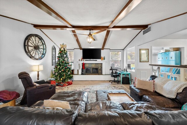 living room with vaulted ceiling with beams, a textured ceiling, and a tiled fireplace