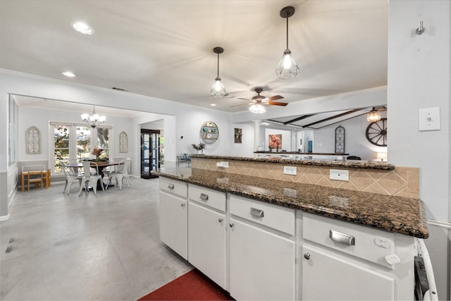 kitchen featuring dark stone countertops, white cabinets, pendant lighting, and ceiling fan with notable chandelier