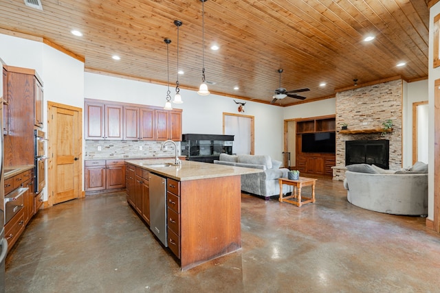 kitchen featuring appliances with stainless steel finishes, decorative light fixtures, tasteful backsplash, a fireplace, and a kitchen island with sink