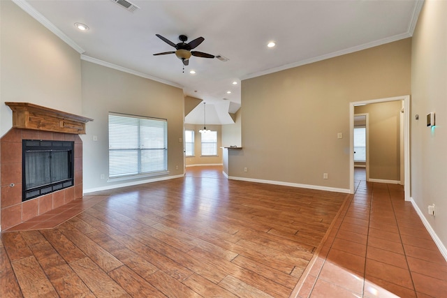 unfurnished living room featuring a tiled fireplace, ceiling fan, ornamental molding, and hardwood / wood-style flooring