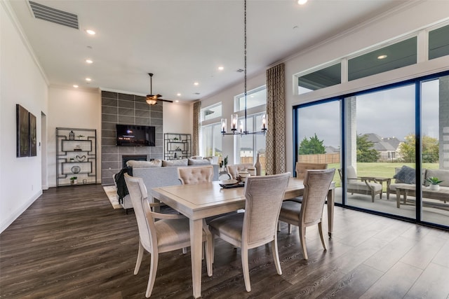 dining area with a tile fireplace, dark hardwood / wood-style floors, ceiling fan with notable chandelier, and ornamental molding