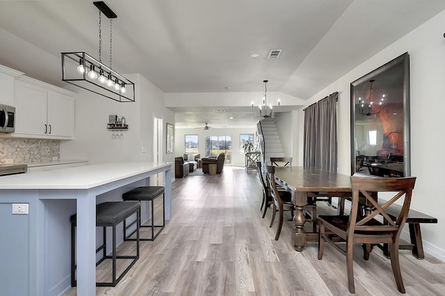 dining space featuring ceiling fan with notable chandelier, vaulted ceiling, and light hardwood / wood-style flooring