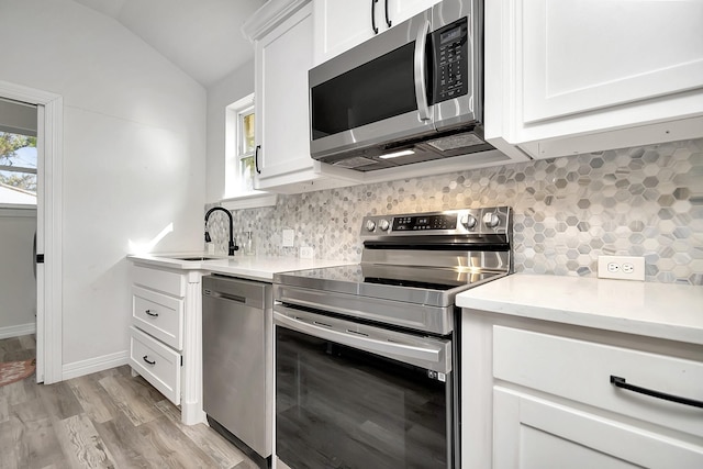 kitchen featuring sink, light hardwood / wood-style floors, vaulted ceiling, white cabinets, and appliances with stainless steel finishes