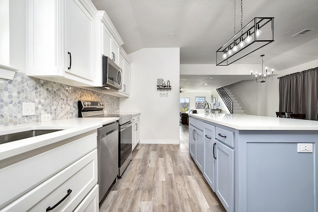 kitchen featuring white cabinets, stainless steel appliances, ceiling fan with notable chandelier, and a kitchen island