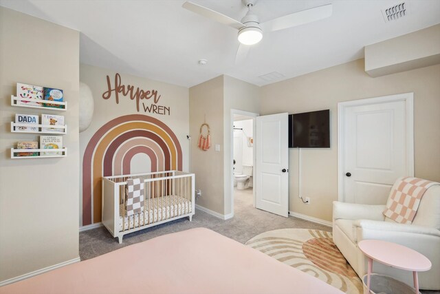 bedroom with carpet, ceiling fan, a crib, and connected bathroom