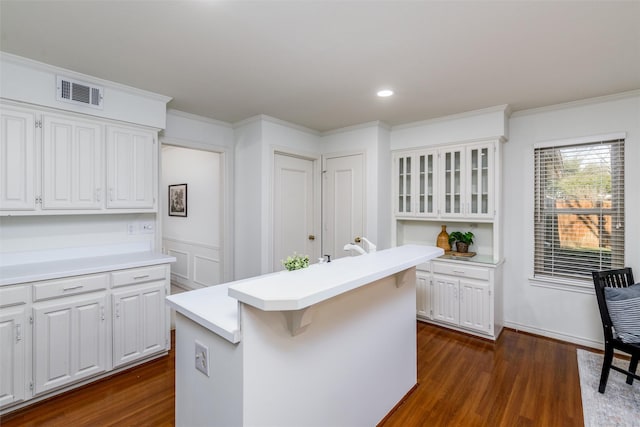 kitchen with a center island, ornamental molding, a kitchen bar, dark hardwood / wood-style floors, and white cabinetry