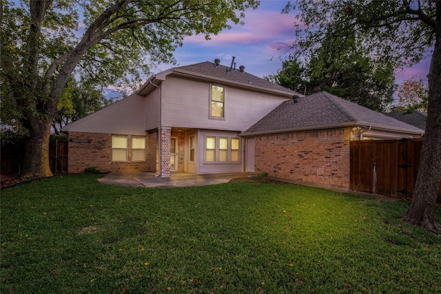 back house at dusk featuring a patio area and a yard