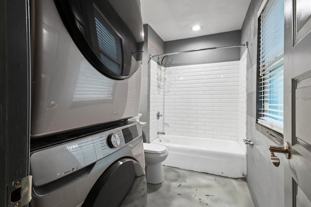 bathroom with stacked washer / drying machine, toilet, concrete flooring, and tiled shower / bath