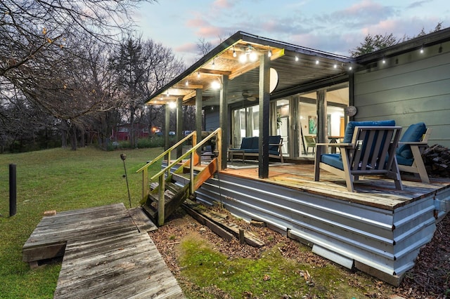 back house at dusk featuring a wooden deck, ceiling fan, and a yard