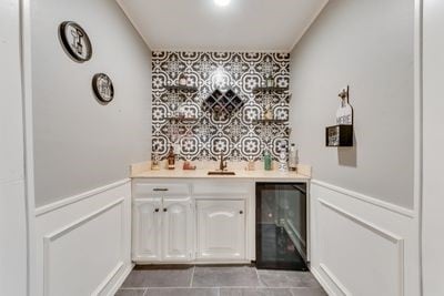 bar featuring beverage cooler, tile patterned flooring, sink, and white cabinets