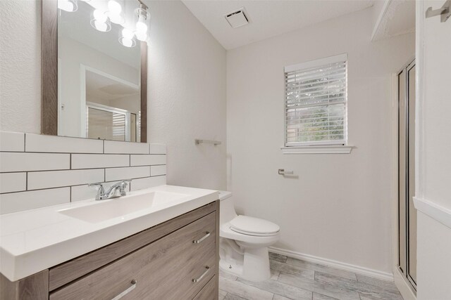 bathroom with hardwood / wood-style floors, vanity, toilet, tasteful backsplash, and a shower with shower door