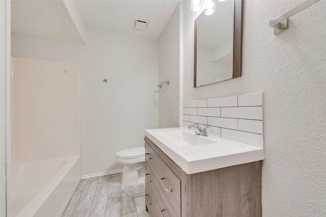 bathroom with tasteful backsplash, vanity, a textured ceiling, wood-type flooring, and toilet