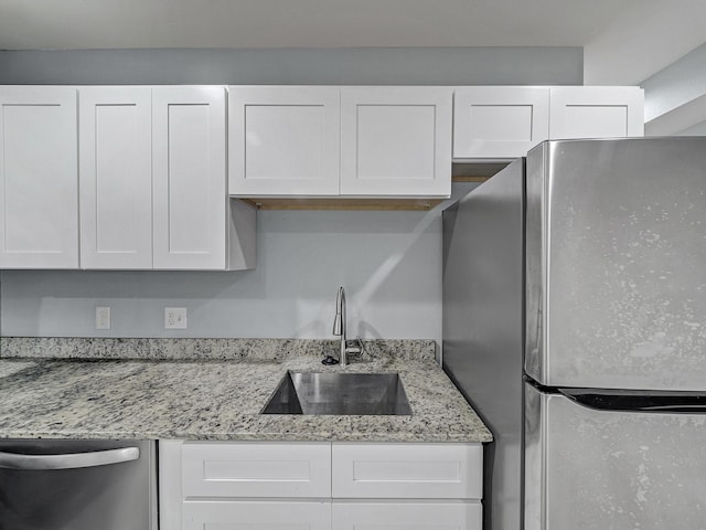 kitchen featuring white cabinets, sink, light stone countertops, and stainless steel appliances