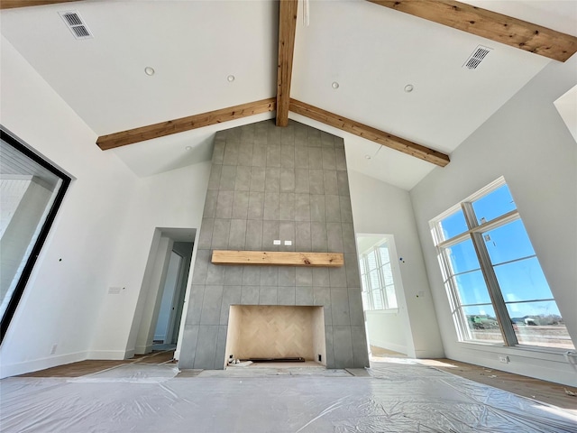 unfurnished living room featuring a tiled fireplace, beam ceiling, and high vaulted ceiling