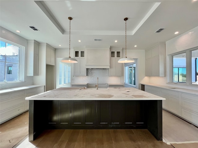 kitchen with a raised ceiling, custom exhaust hood, and a large island with sink