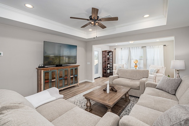 living room featuring hardwood / wood-style flooring, ceiling fan, crown molding, and a tray ceiling