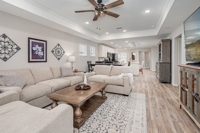 living room with a raised ceiling, ceiling fan, crown molding, and light hardwood / wood-style floors