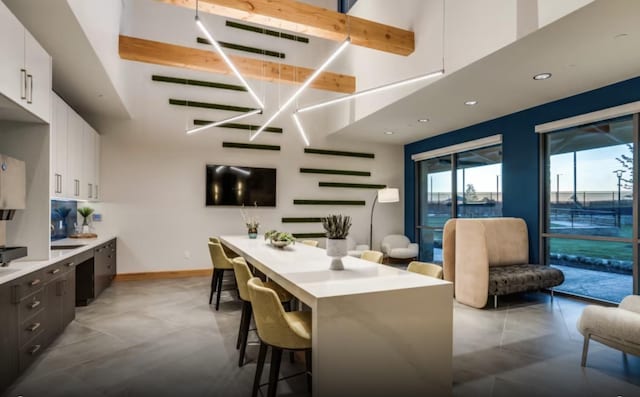 kitchen featuring a breakfast bar area, dark brown cabinetry, a towering ceiling, and white cabinets