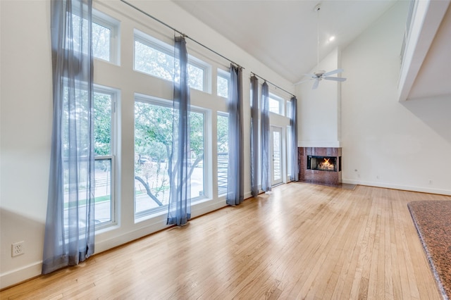 unfurnished living room featuring a fireplace, high vaulted ceiling, light hardwood / wood-style floors, and a healthy amount of sunlight