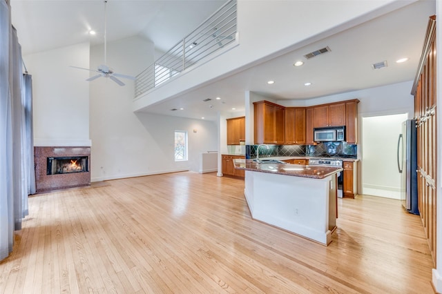 kitchen with dark stone counters, high vaulted ceiling, stainless steel appliances, and light wood-type flooring