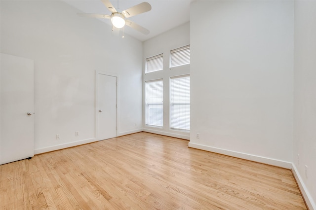 empty room featuring a towering ceiling, light hardwood / wood-style flooring, and ceiling fan