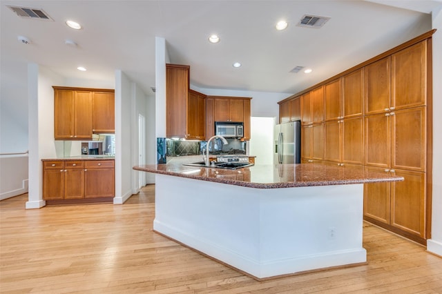 kitchen with dark stone counters, sink, light wood-type flooring, and appliances with stainless steel finishes