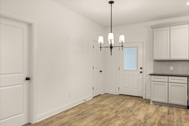 unfurnished dining area featuring an inviting chandelier and light wood-type flooring