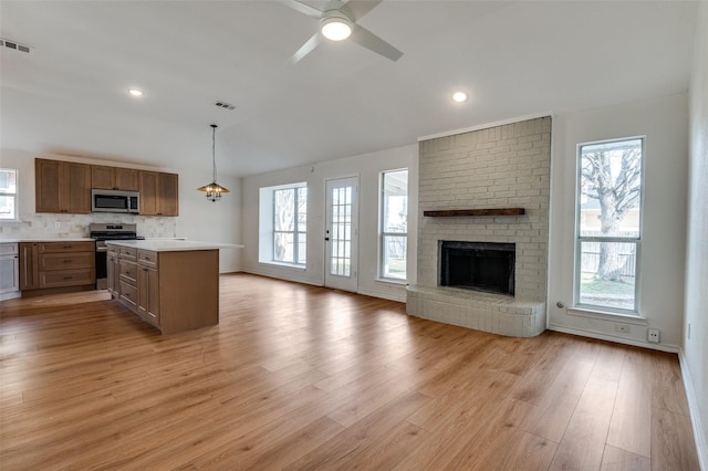 kitchen featuring a brick fireplace, stainless steel appliances, decorative light fixtures, light hardwood / wood-style flooring, and a center island